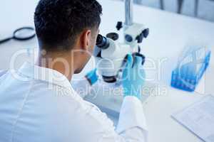 Working on a breakthrough thatll change the world. Rearview shot of a young man using a microscope in a lab.