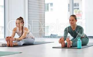 Feel the stretch in your hamstrings. Full length shot of two young women practising yoga in the studio and holding a seated forward fold pose.