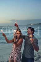 happy couple holding sparklers celebrating new years eve on beach at sunset with sparkle firework