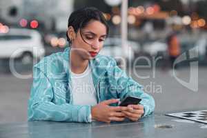 Sad, depressed and stressed female with mental health problem texting on phone while sitting at outdoor cafe. Young woman getting negative response or bad news while chatting or browsing social media