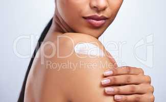 Lotion like a potion. an unrecognizable woman applying moisturiser to her shoulder against a grey background.