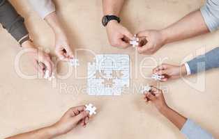 Every individual has their role to play. High angle shot of an unrecognizable group of businesspeople huddled together and doing a puzzle in the office.