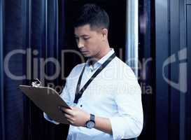 In the world of tech, he knows whats up. a young man making notes while working in a server room.