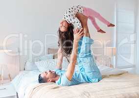 Wake up and have a fun-filled day. a man lying on a bed and lifting his daughter in the air with his feet.