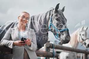 Fresh air and back rides. Portrait of an attractive woman using her cellphone while posing with a horse in an enclosed pasture on a farm.