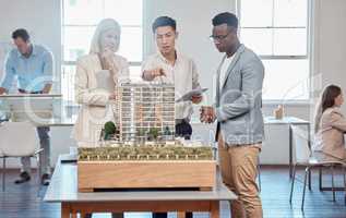 Diverse architects or project managers discuss floor plan of building expansion. Asian engineer presents blueprint and 3D model for a new office to Caucasian and African American clients.