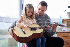 Teaching her some chords. a young father teaching his daughter to play the guitar at home.