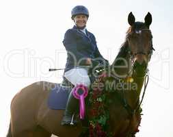 Victory is ours. an attractive young female jockey sitting on her horses back in the winners circle.