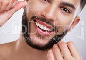 My smile is my winning feature. a young man flossing his teeth against a studio background.