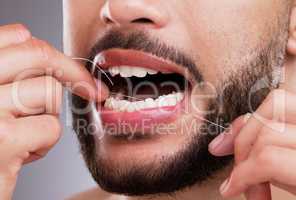 Be thorough when flossing. a man flossing his teeth against a studio background.