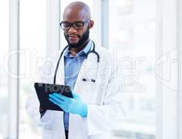 Getting ready for a busy day at the clinic. a handsome young doctor standing alone in his clinic and using a digital tablet.