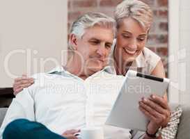 Thankful to have found you. a mature couple using a digital tablet at home on the sofa together.