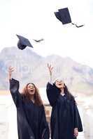 The harder you work, the higher the reward. two young women throwing their caps in the air on graduation day.