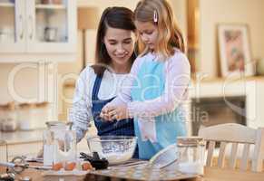 Only two eggs are needed. a young woman helping her daughter crack eggs into a bowl.