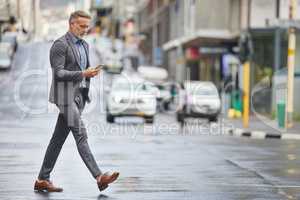 This work needs to get done soon. a handsome businessman walking through the city while using his smartphone.