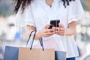 Hold on, Im coming with my credit card now. a woman using a smartphone while shopping against an urban background.
