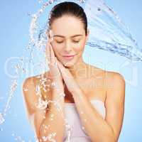Water is your best friend. a young woman washing her face against a blue background.