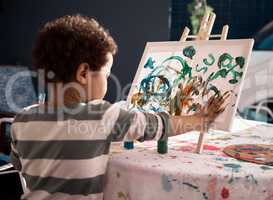 Sensory play encourages learning through curiosity and creativity. a little boy painting on a canvas.