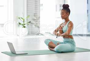 Following a guided meditation. Full length shot of an attractive young woman sitting with her legs crossed and following an online yoga class.