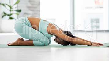 A great stretch for the upper back. Full length shot of a young woman practising yoga in the studio alone and holding a childs pose.