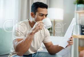 I need coffee to think. a young man sitting in his living room and enjoying a cup of coffee while calculating his finances.