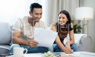 Well done on saving this month, babe. a young couple sitting together in their living room at home and calculating their finances.