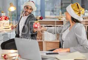 We might be working but well still have a jolly time. a young businessman and businesswoman exchanging Christmas gifts in a modern office.