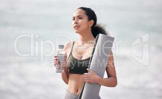 Yoga keeps me zen-tered. a fit young woman holding her yoga mat and water bottle while at the beach.