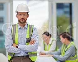 I trust my team completely. Cropped portrait of a handsome young male construction worker standing with his arms folded with his colleagues in the background.