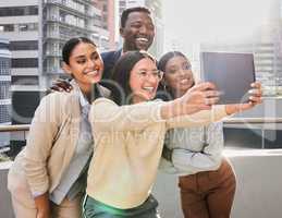 Smile, gang. a group of young businesspeople using a tablet to take selfies on an office balcony.