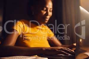 Woman freelancer working remote on a laptop while typing and answering emails online. Smiling, positive black female entrepreneur completing a project late at night while sitting at a desk at home