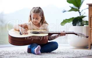 Shes found a new hobby. a little girl playing a guitar at home.