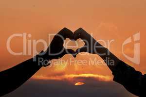 I need you like a heart needs a beat. an unidentifiable couple making a heart shape with their hands at sunset.