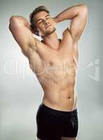 Swoon and stare all you want. Studio shot of a muscular young man posing against a grey background.