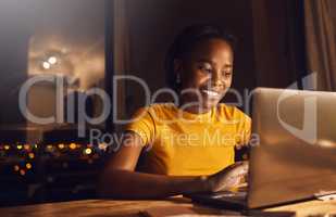 Young, happy and beautiful woman working and studying at night to make deadline for online course. Smiling and positive student using a laptop to finish her project while sitting at her desk at home