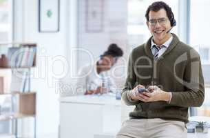 Hes always busy making a connection. Portrait of a young businessman wearing a headset and using a cellphone while working in an office.