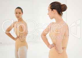 A human being can survive almost anything. a young ballet dancer inspecting her figure in a mirror during a rehearsal.