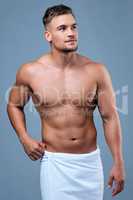 Always grateful, never satisfied. Studio shot of a muscular young man posing in a towel against a grey background.