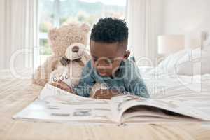 Broadening his imagination. Full length shot of an adorable little boy reading a book on a bed at home.