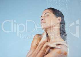 This is totally relaxing and refreshing. Studio shot of an attractive young woman taking a shower against a blue background.