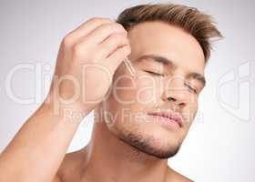 Clear skin takes patience. Studio shot of a young man applying serum to his face against a grey background.