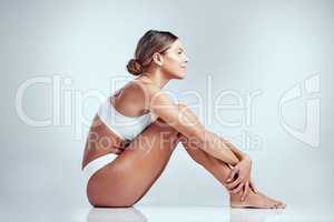 The picture of contentment. Studio shot of an attractive young woman sitting on the floor against a grey background.