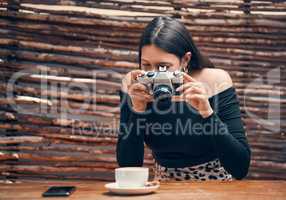 Stylish, trendy and creative food influencer taking a picture with a camera of a cup of coffee for her blog in a cafe shop. Young female content creator taking a photo for her blog website at a cafe