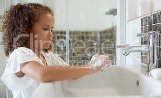 Little girl washing hands with water and soap in bathroom at home. Learning about and practicing good hygiene keeps us healthy. Child cleaning fingers at a basin or sink