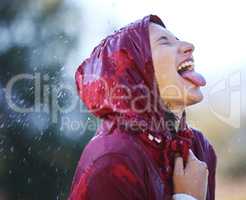 Carefree in the rain. a young woman sticking out her tongue to feel the rain outside.