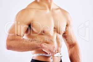 Finally exactly where I want to be. a male athlete measuring his waist against a white studio background.