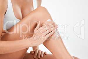Take care of the skin youre in. a woman applying lotion to her legs against a studio background.