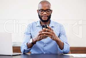 I should inform the rest of the team. a young businessman using his cellphone while sitting at his desk.