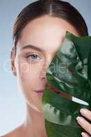 Keeping it natural. Studio portrait of an attractive young woman posing with a palm leaf against a grey background.