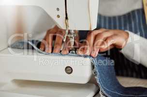 Close up hands of a professional female designer sitting on a sewing machine in her studio. Process of a tailor at work on repairing and designing clothes. Casual alterations being done to jeans.